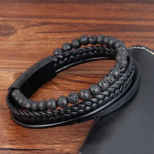 Pulsera de cuero de tres tiras una de ella trenzada y otra con piedras volcánicas y cierre de acero en color negro